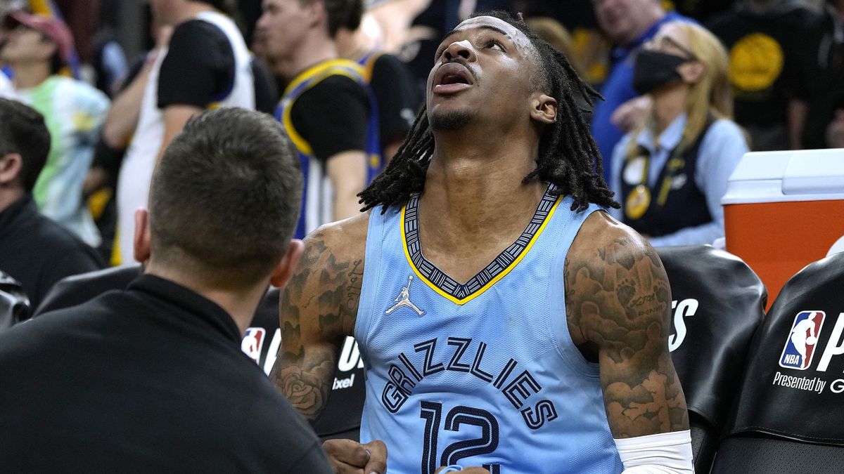 a Morant #12 of the Memphis Grizzlies sits on the bench and reacts after a team trainer examines
