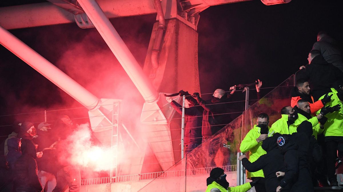Supporters and security staff members react near a flare during the French Cup round of 64 football match between Paris FC and Olympique Lyonnais (OL) at the Charlety stadium in Paris, on December 17, 2021. - The match was interrupted due to incidents in