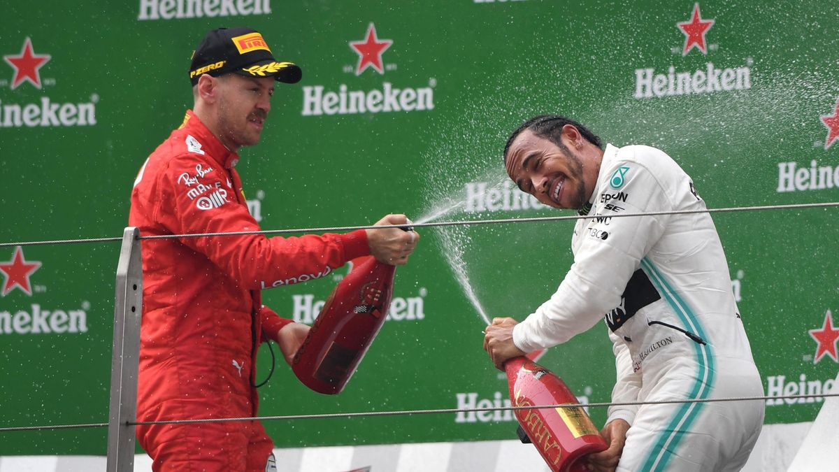 Third-placed Ferrari's German driver Sebastian Vettel (L) sprays champagne at winner Mercedes' British driver Lewis Hamilton (R)