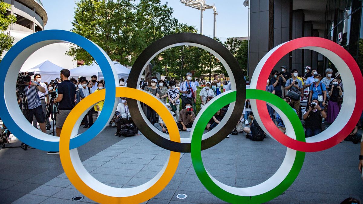 Des personnes masquées derrière les anneaux olympiques, à Tokyo, le 21 juillet 2021