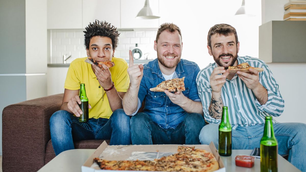 Amici che bevono birra, mangiano pizza a casa e guardano la partita sportiva