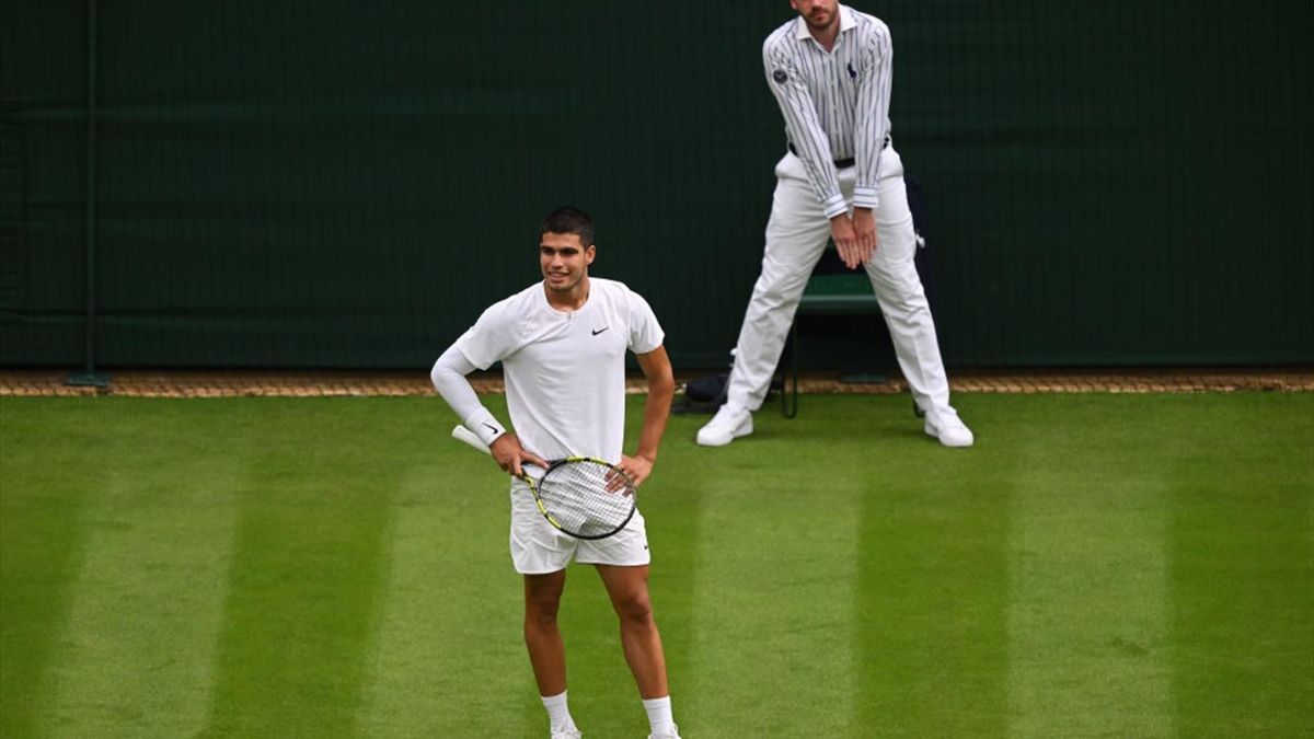 Een lijnrechter geeft de bal in op Wimbledon, Carlos Alcaraz kijkt toe.