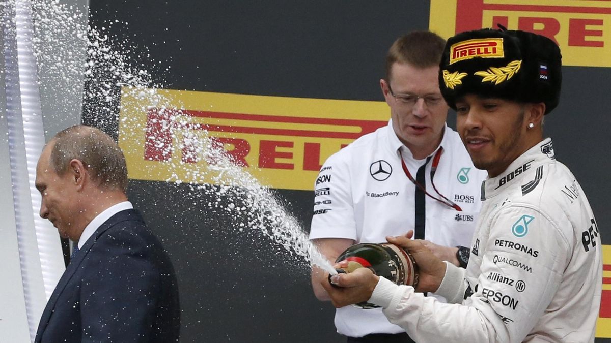 Russian President Vladimir Putin (L) leaves the winners podium as Mercedes Formula One driver Lewis Hamilton of Britain (R) sprays champagne in celebration after winning the Russian F1 Grand Prix in Sochi, Russia, October 11, 2015. Hamilton won the race a